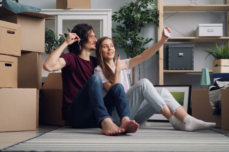 VA Home - 1 27 Young couple sitting among moving boxes taking a selfie cele 1791306358